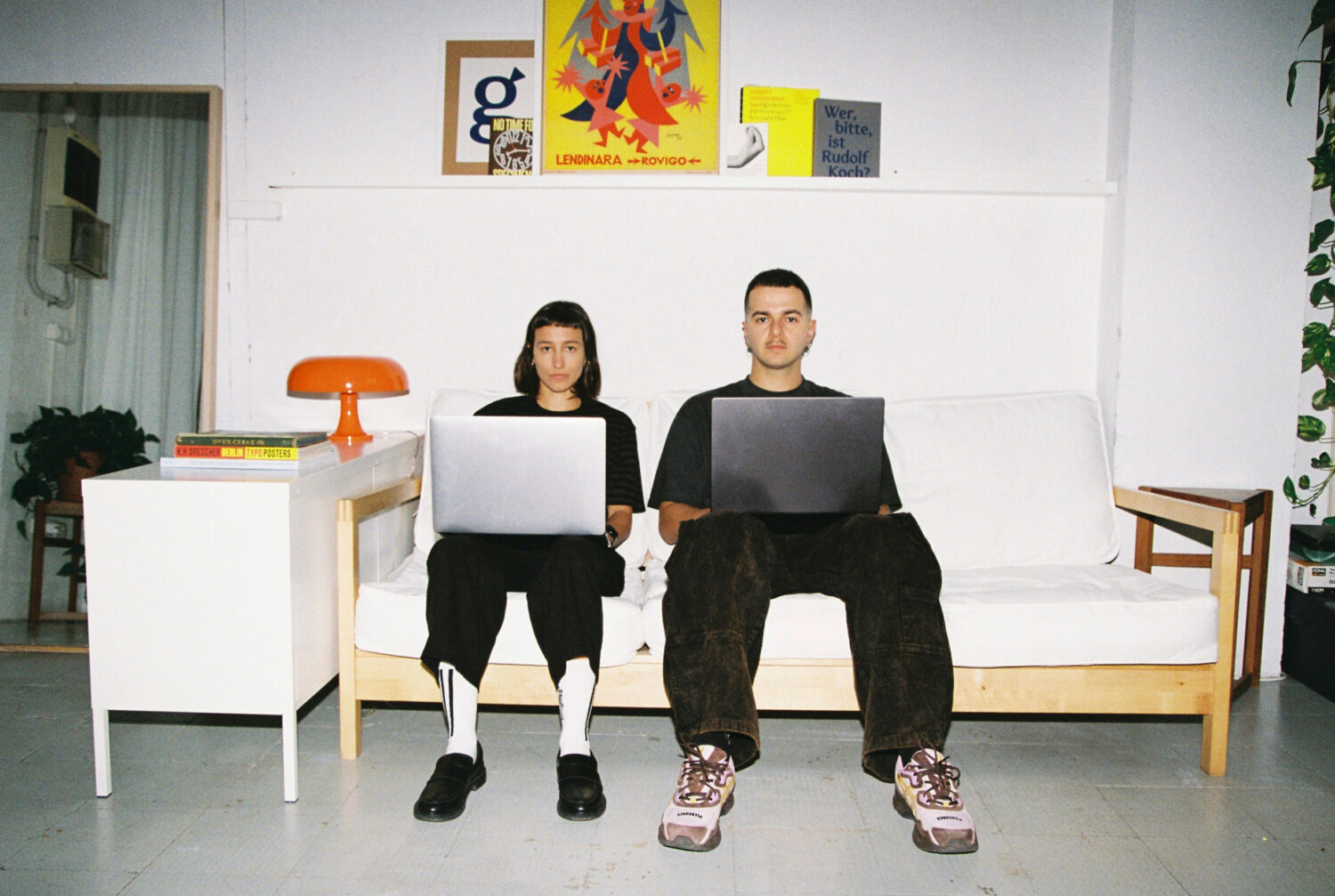 Two people sitting on a light wooden sofa with laptops on their laps